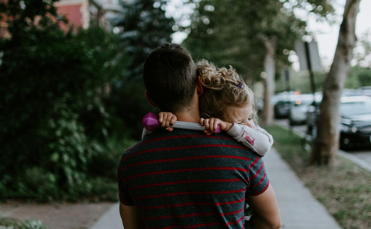 Rear shot of father carrying sleeping toddler daughter down the sidewalk